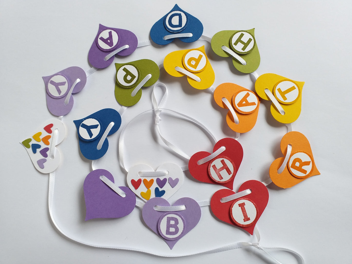 Colorful heart-shaped letter cookies on a white plate with balloons and streamers in the background.
