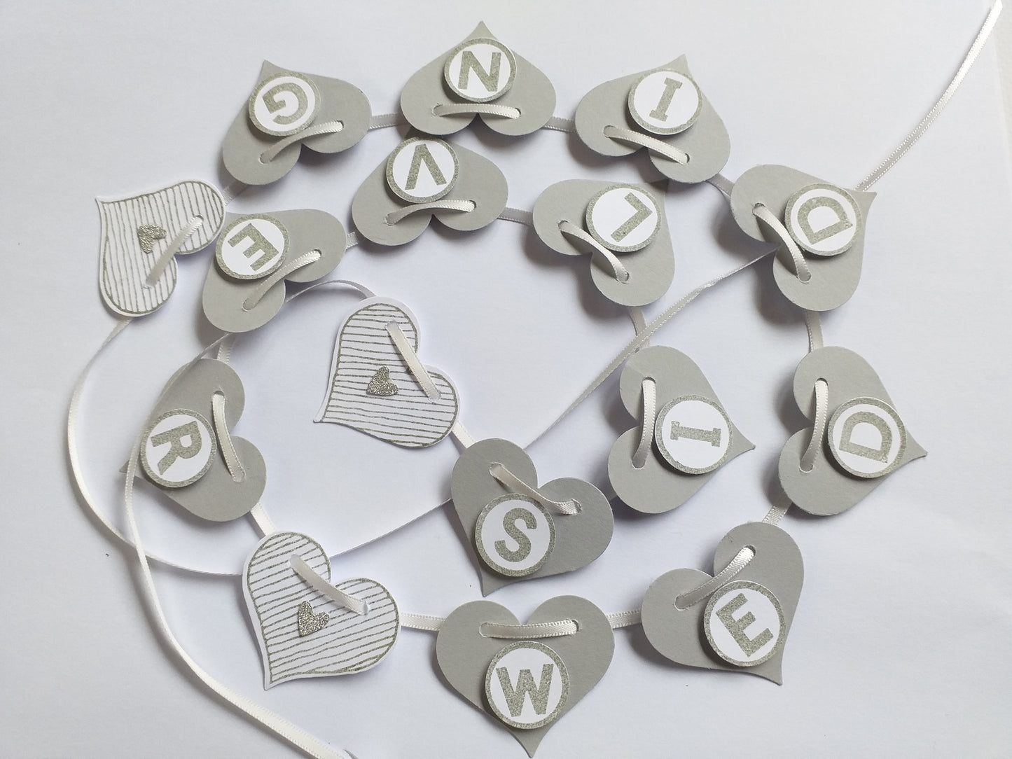 Handcrafted silver wedding banner with heart shapes and letters spelling out 'Silver Wedding' on a satin ribbon.