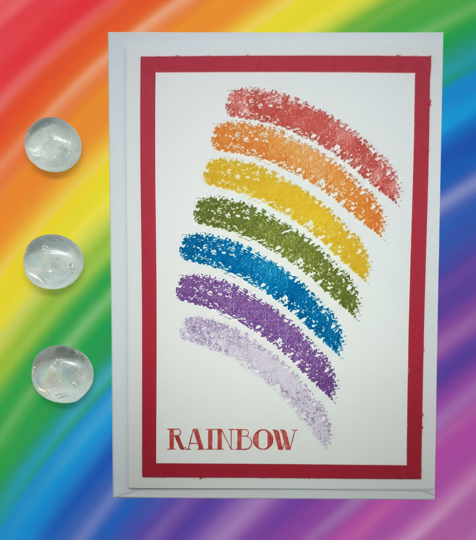 A colorful hand-stamped greeting card with a rainbow design on a red background, with a white border and text label 'RAINBOW'.