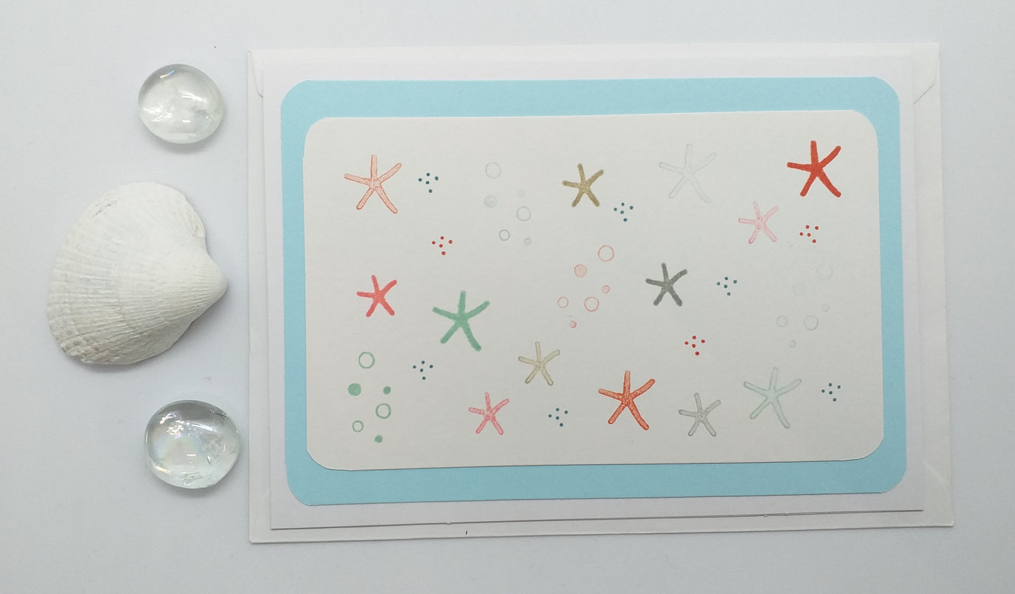 A hand-stamped greeting card with a layered design featuring multiple colored starfish, accompanied by an envelope.