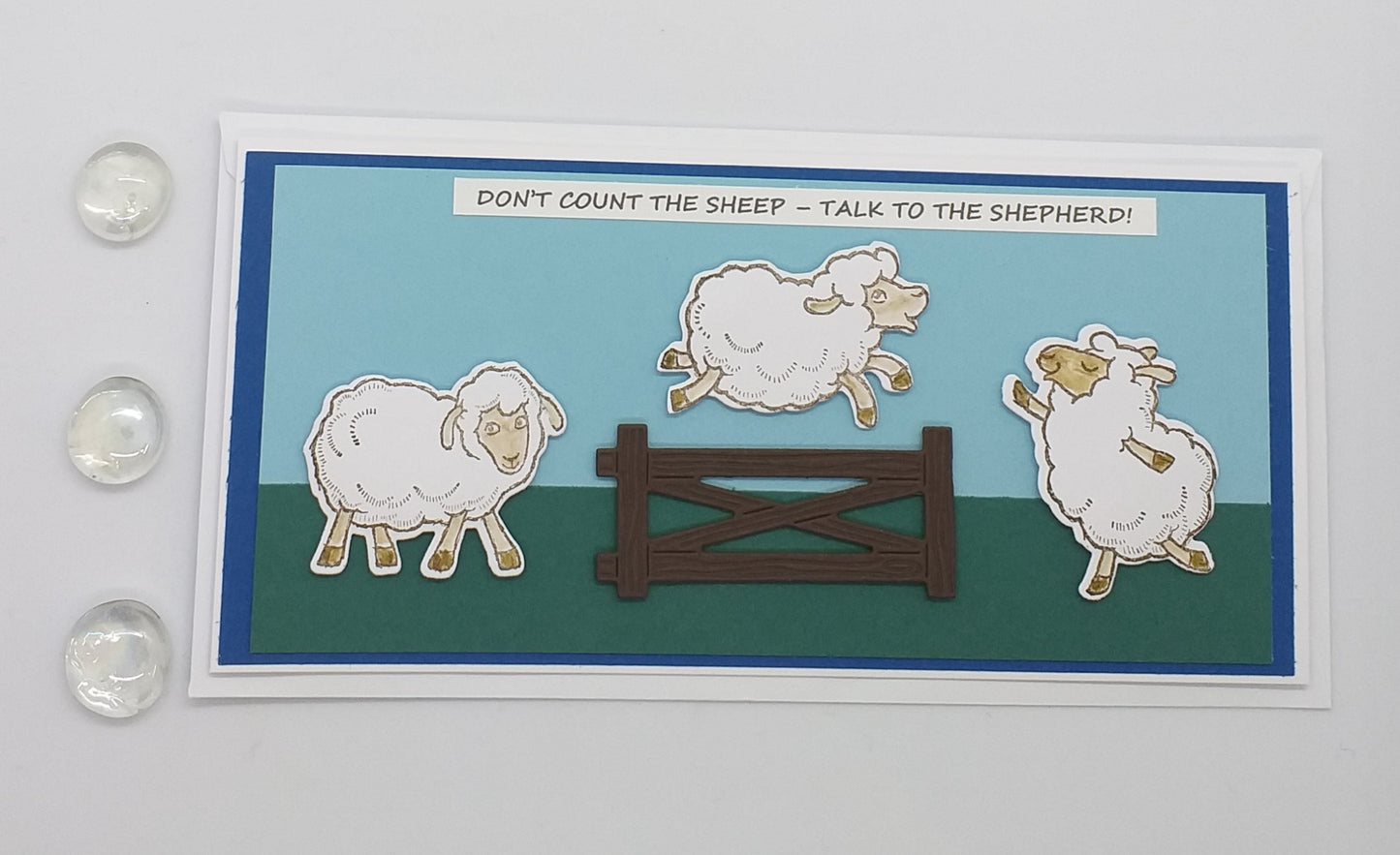 A colorful card with sheep illustrations and a wooden gate die cut, with a religious message encouraging communication with God.