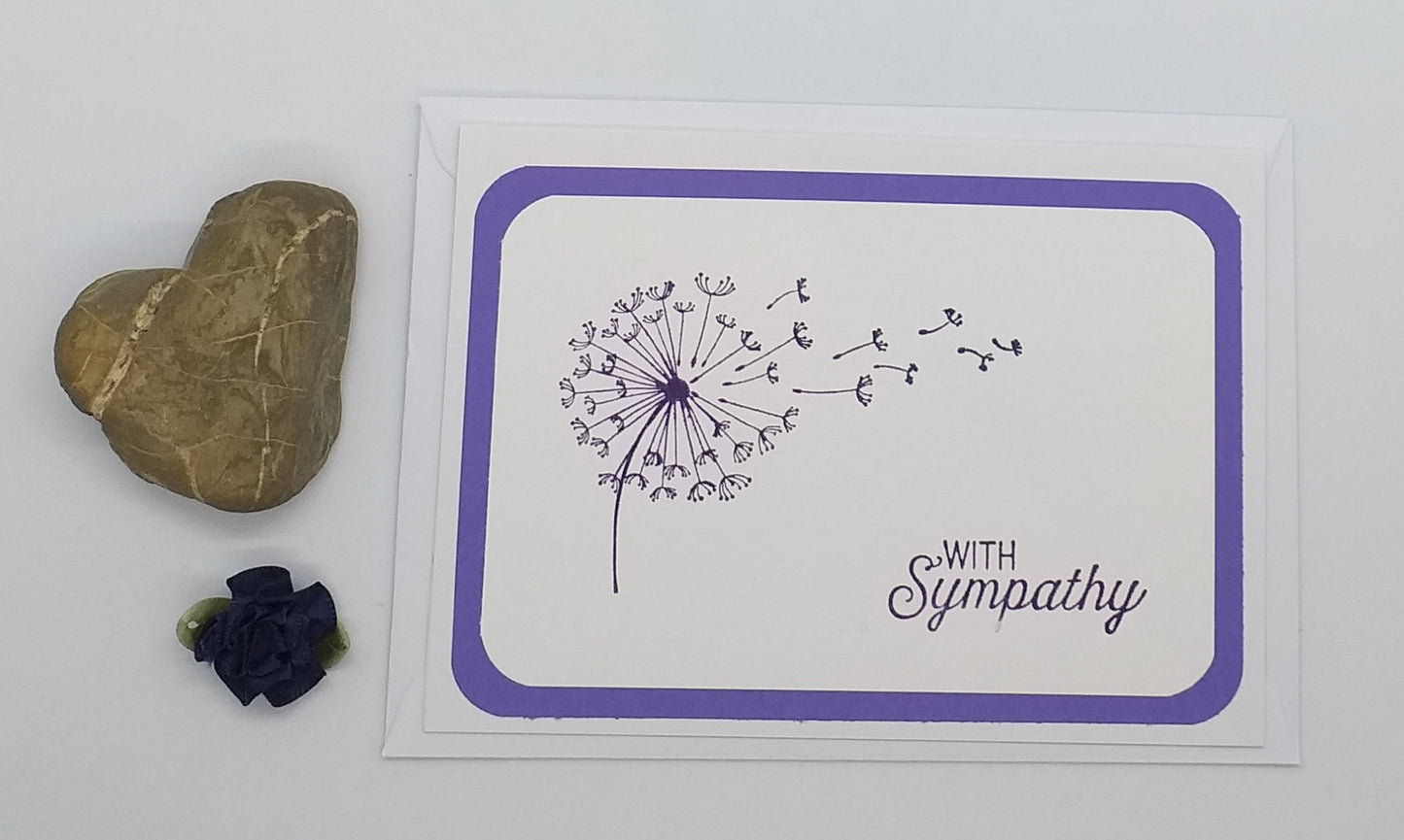 Sympathy card with dandelion illustration and heart-shaped stone on floral background