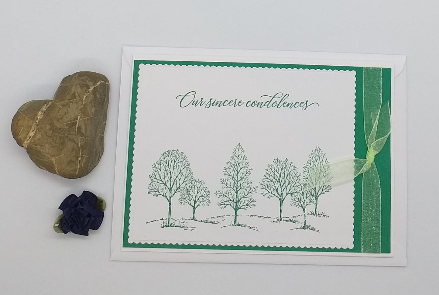 A condolence card with a green and white color scheme, featuring a forest-themed design, accompanied by an envelope and a decorative ribbon.