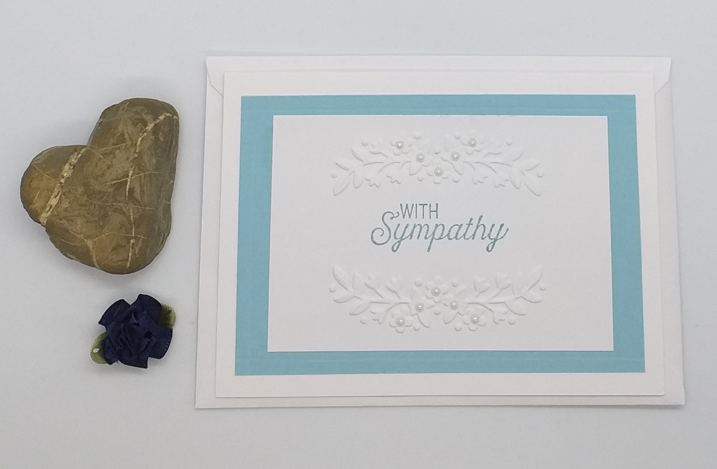 Card with 'With Sympathy' text on a floral background with stones and a flower.