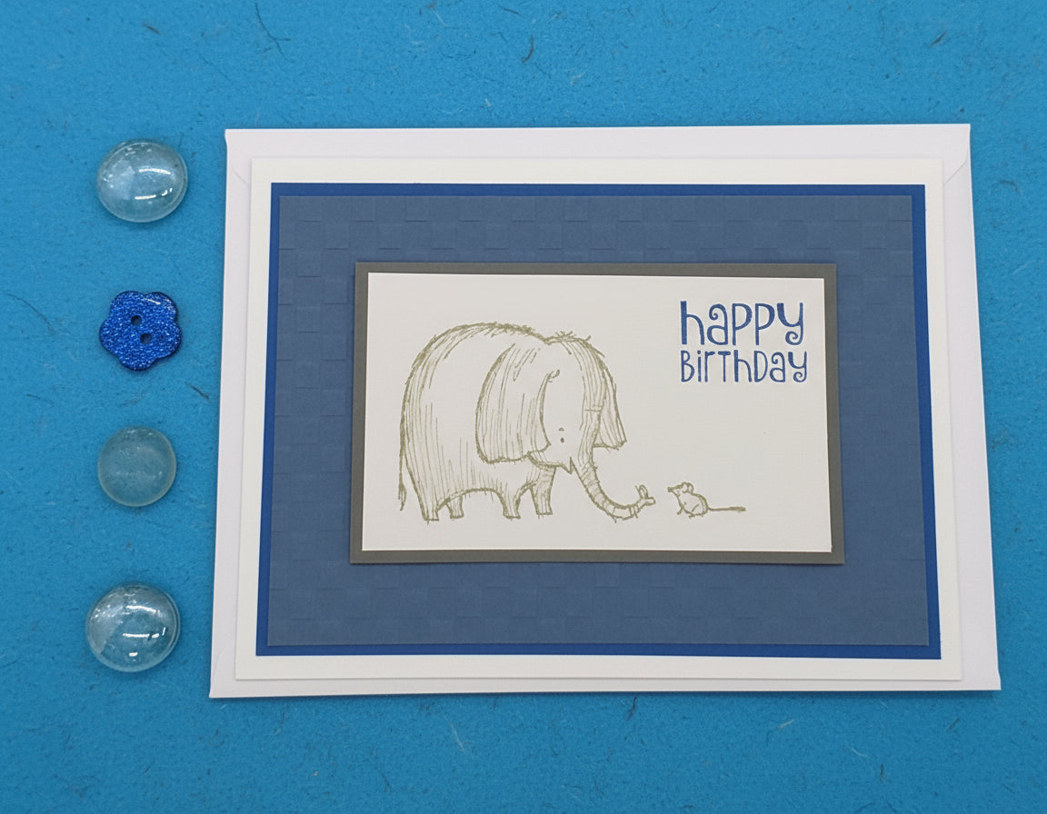 A hand-stamped and layered birthday card with an illustration of an elephant and mouse, and the text 'Happy Birthday' on a blue background.