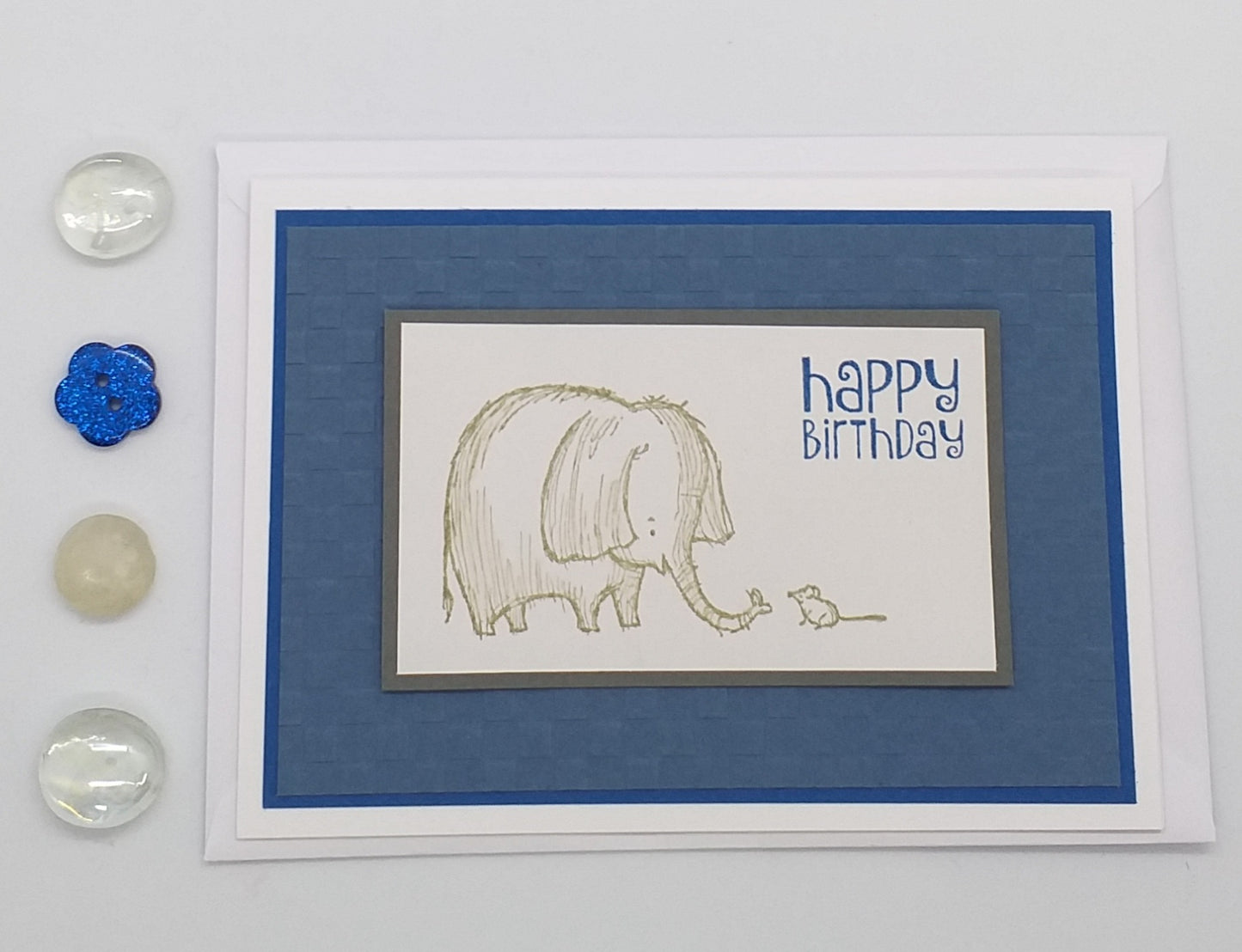 A hand-stamped and layered birthday card with an illustration of an elephant and mouse, and the text 'Happy Birthday' on a blue background.