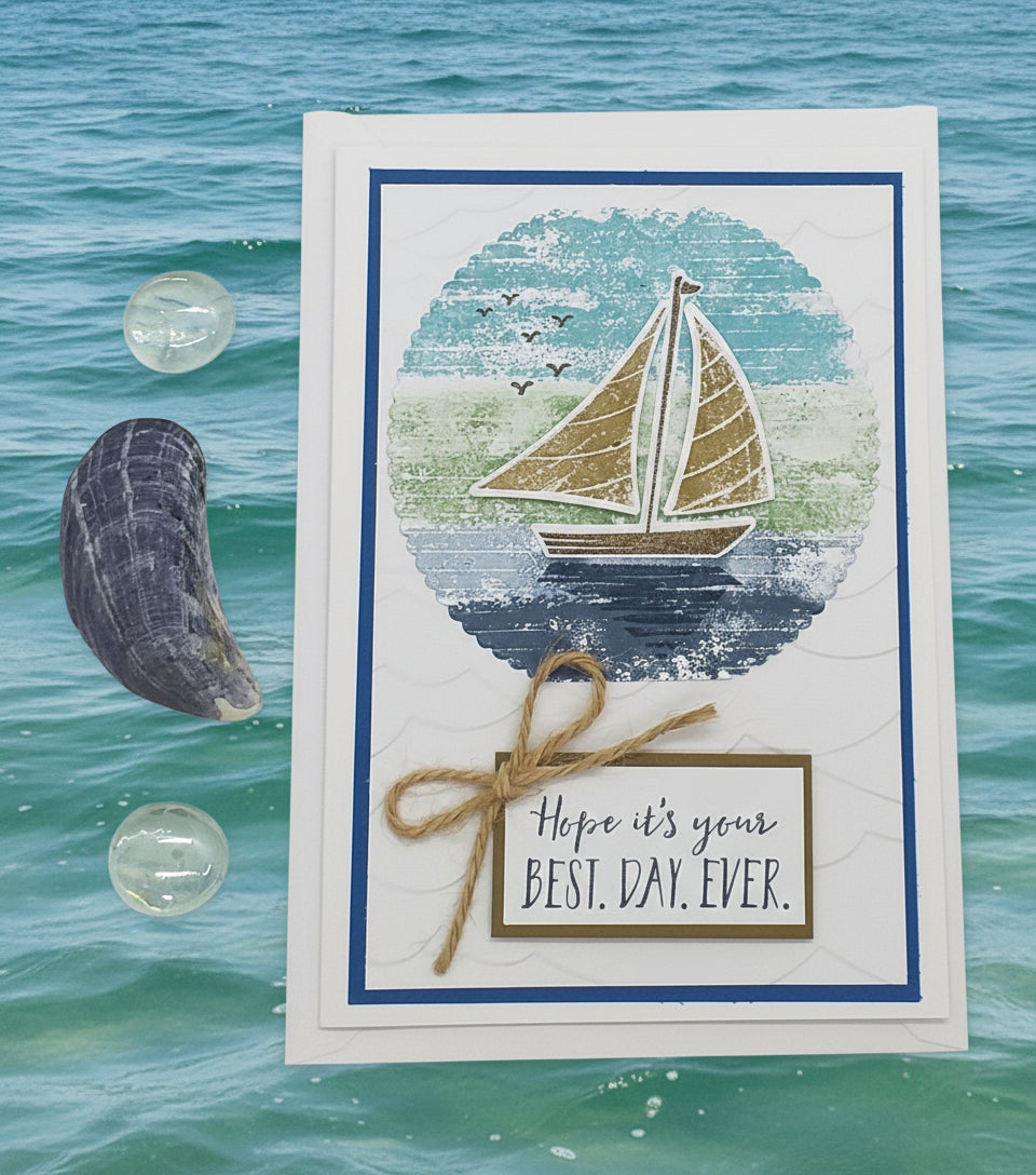 Greeting card with sailboat design and 'Hope it's your best day ever' text, placed on a beach with ocean view.