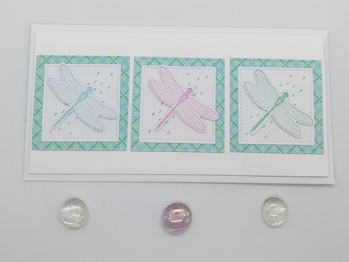 A card with three dragonfly designs, each in different colors, on a green background with a rainbow-colored border.