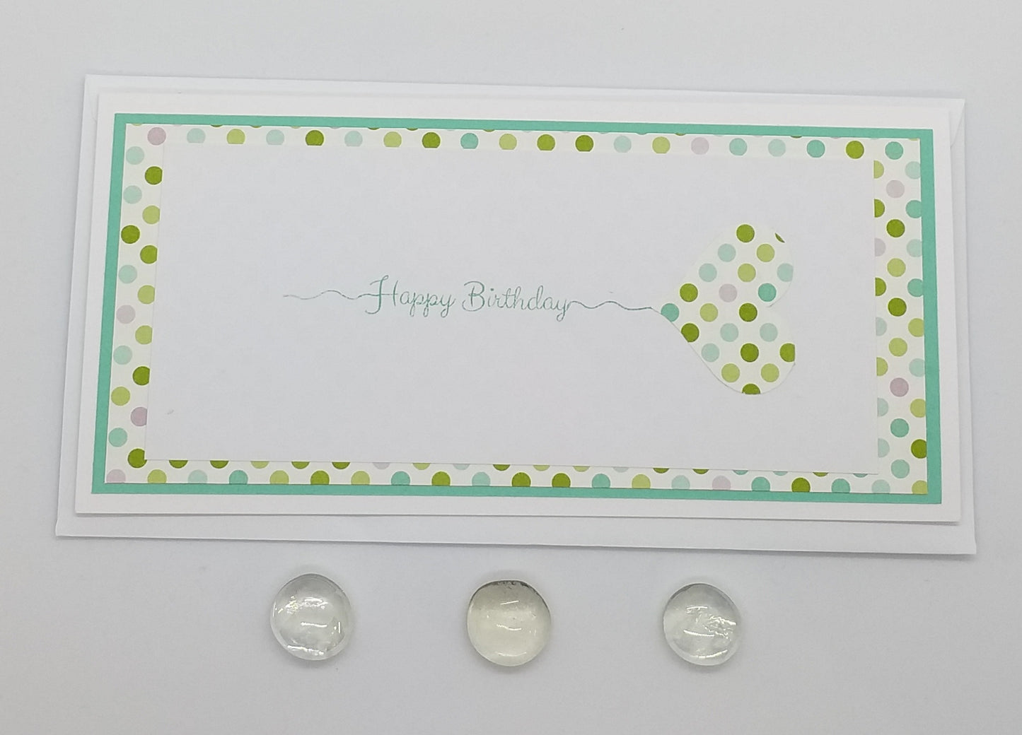A slimline, colorful birthday card with a stamped design, featuring a white background with green and turquoise accents, and a heart-shaped graphic in the center.