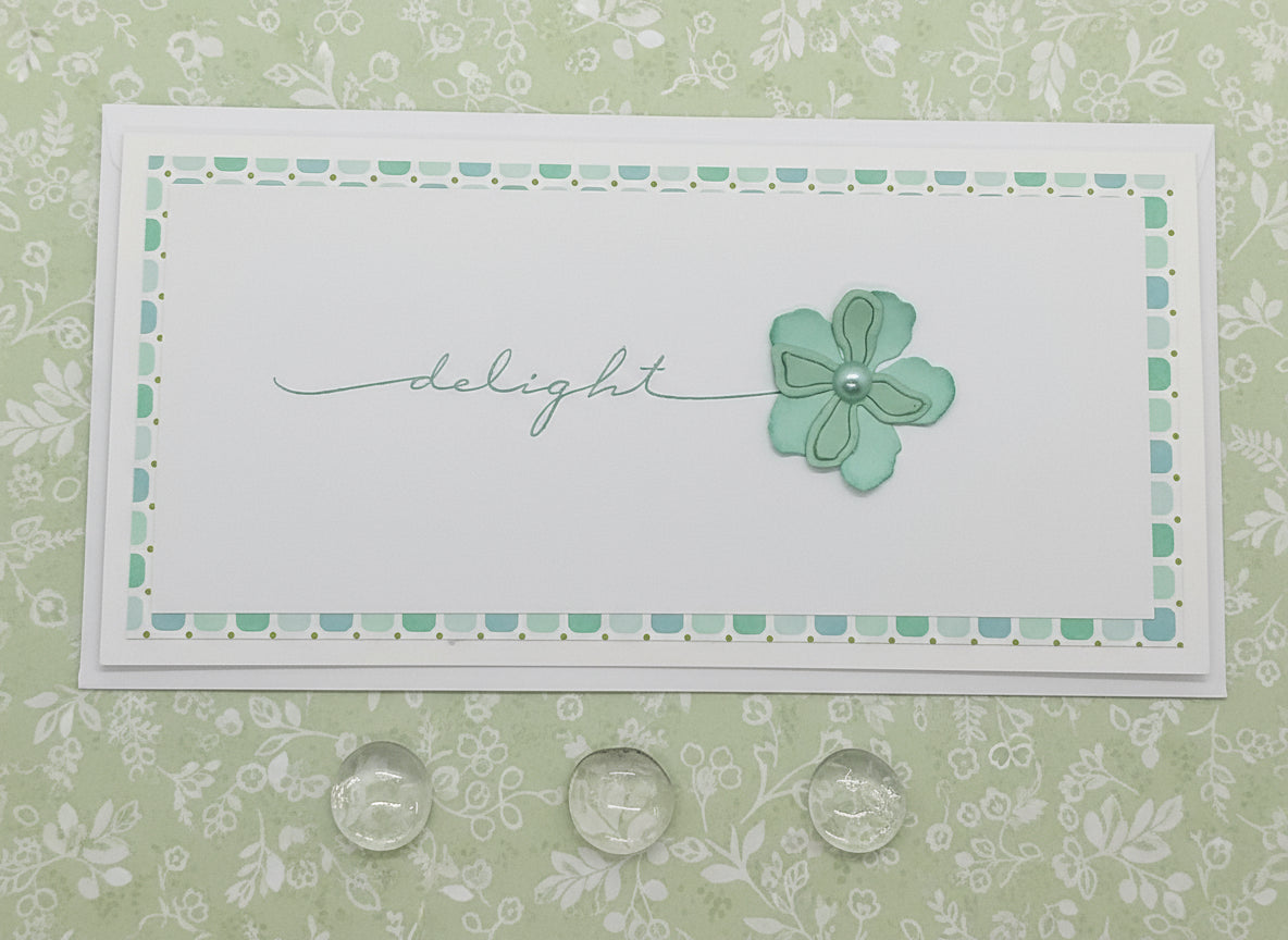 A slimline greeting card with a floral cutout design and the word 'DELIGHT' written on it, accompanied by an envelope.