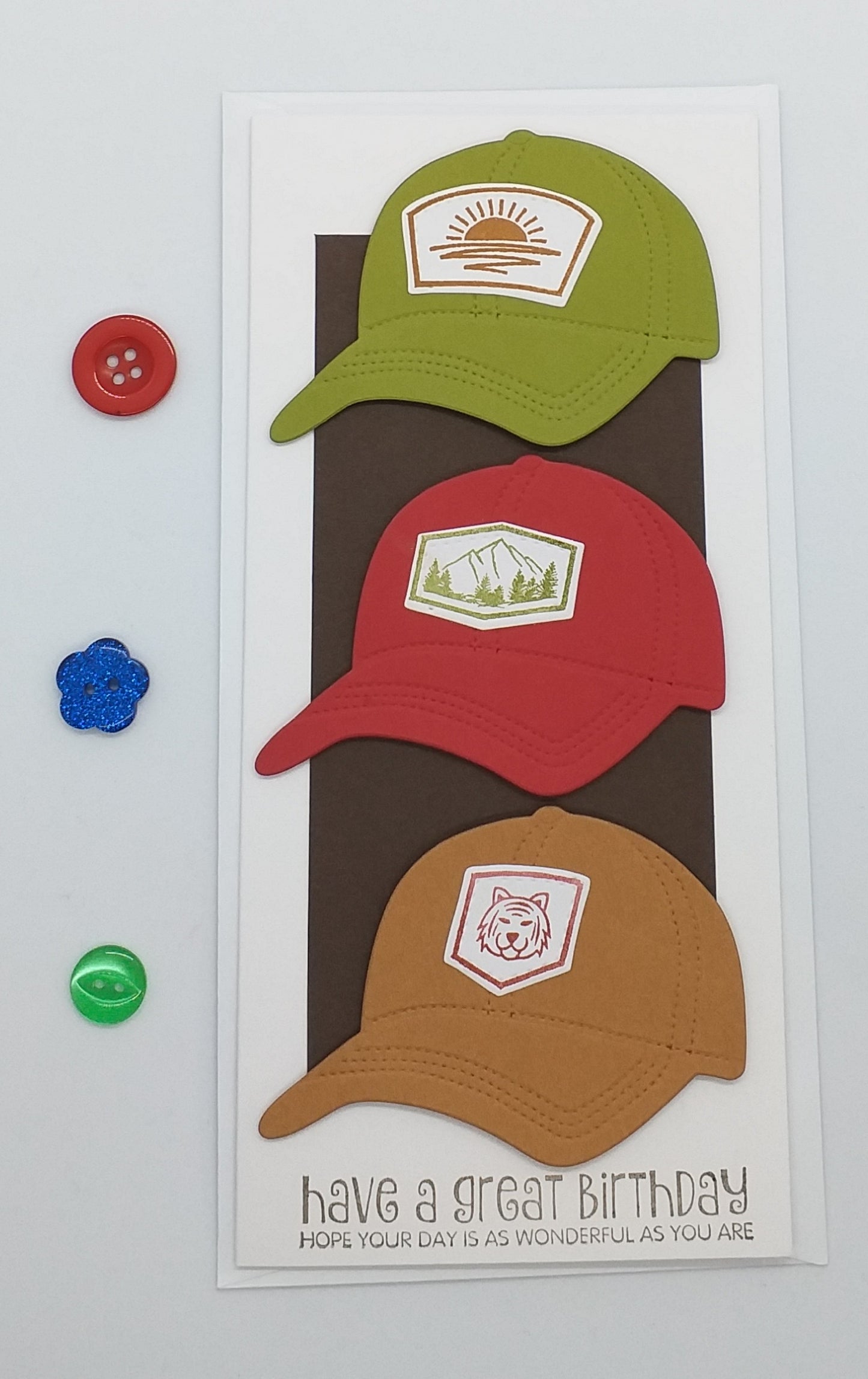 Three colorful baseball caps on a birthday card with decorative buttons on grass