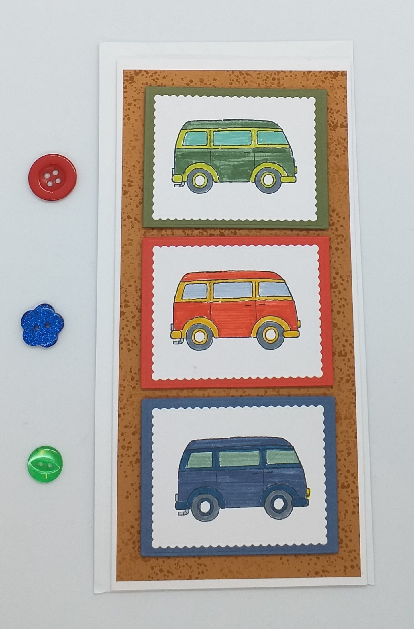 A card with three hand-stamped images of campervans in red, blue, and green on a white background, accompanied by an envelope.