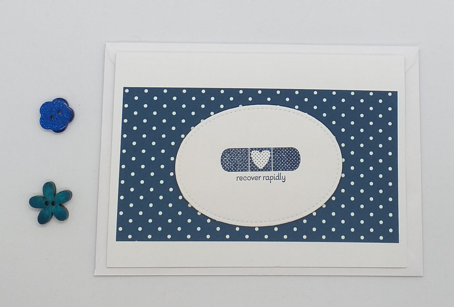 Card with bandage design and 'recover rapidly' text on a blue polka dot background, with decorative flowers on a light gray background.