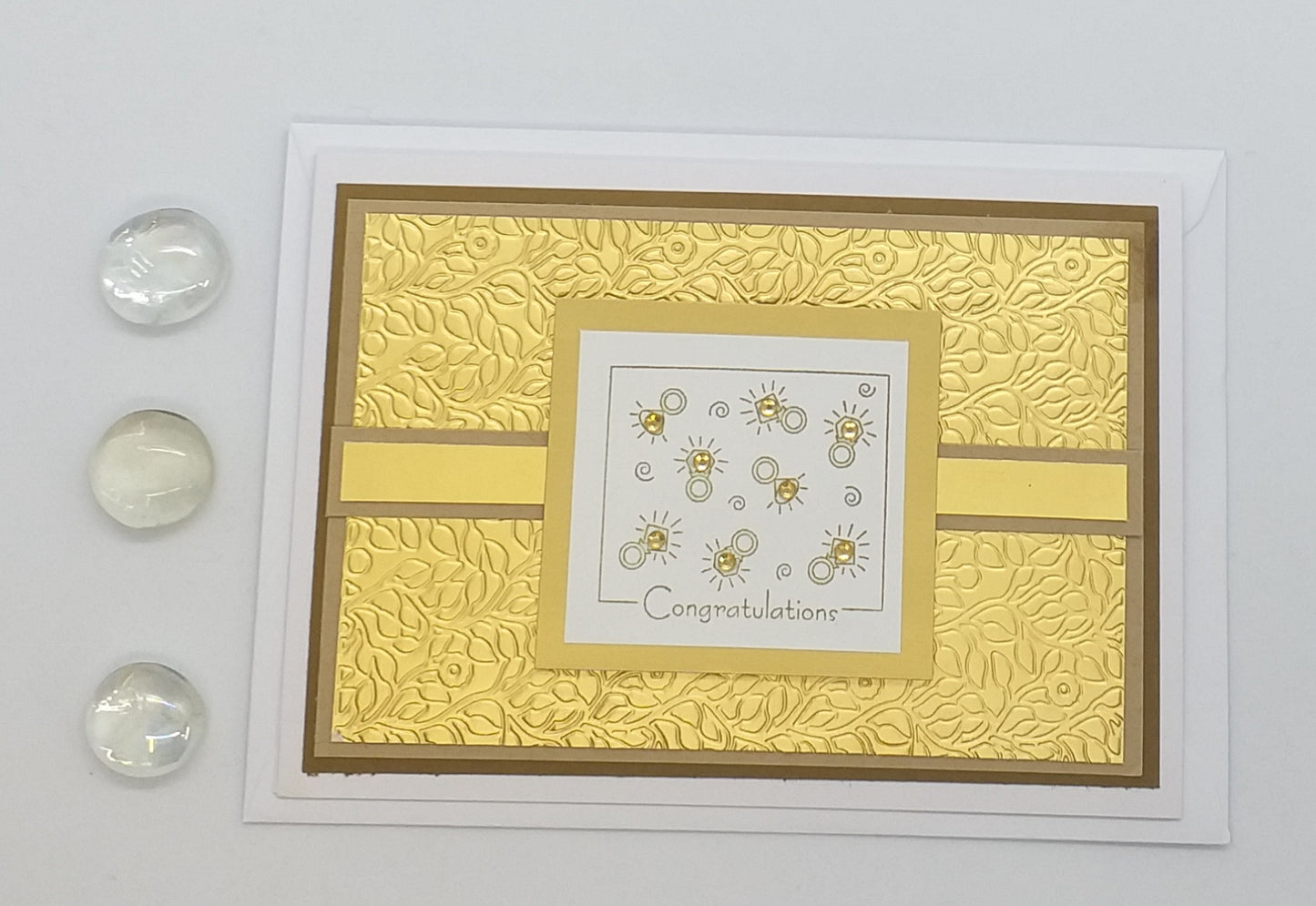 A gold embossed engagement card with floral patterns and gemstone accents, paired with an envelope.