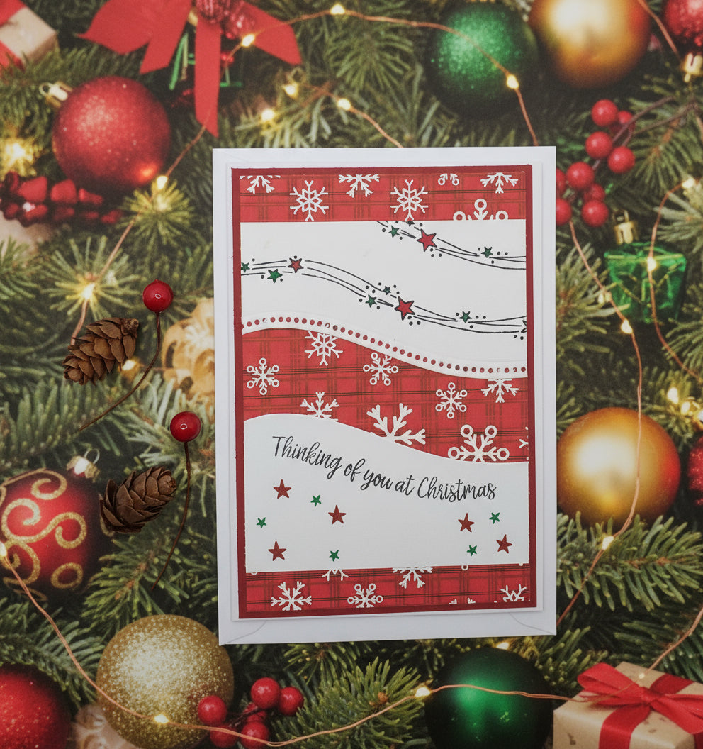 A red and white Christmas card with a 'Thinking of You at Christmas' message, decorated with stars, snowflakes, and a pine cone design.