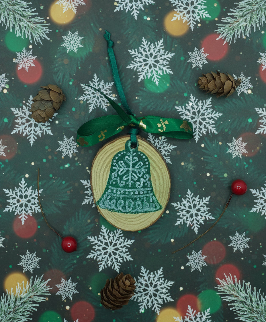A decorative wood slice with a green bell pattern, accompanied by a hanging ribbon and red berries, against a white background with pine needles.