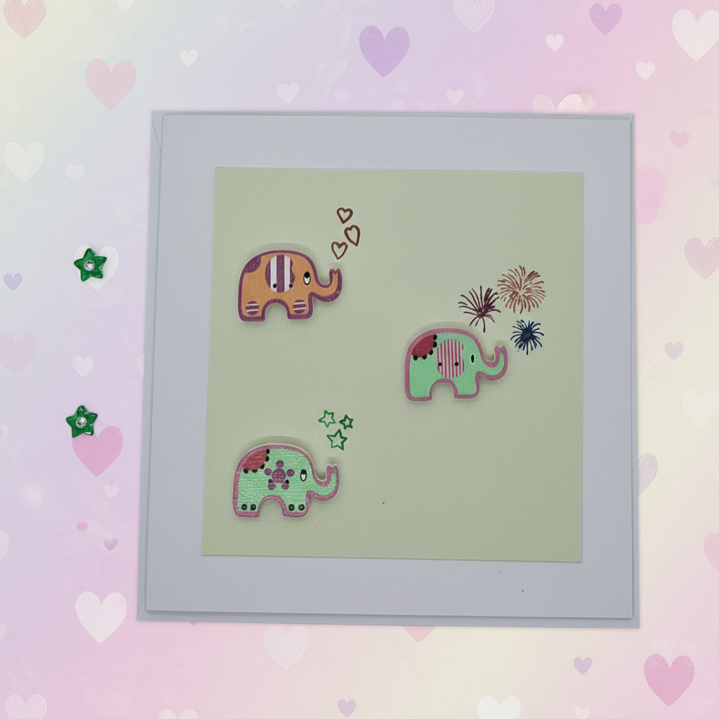 A hand-stamped and layered greeting card with three colorful elephant buttons on a green background, accompanied by small decorative elements.