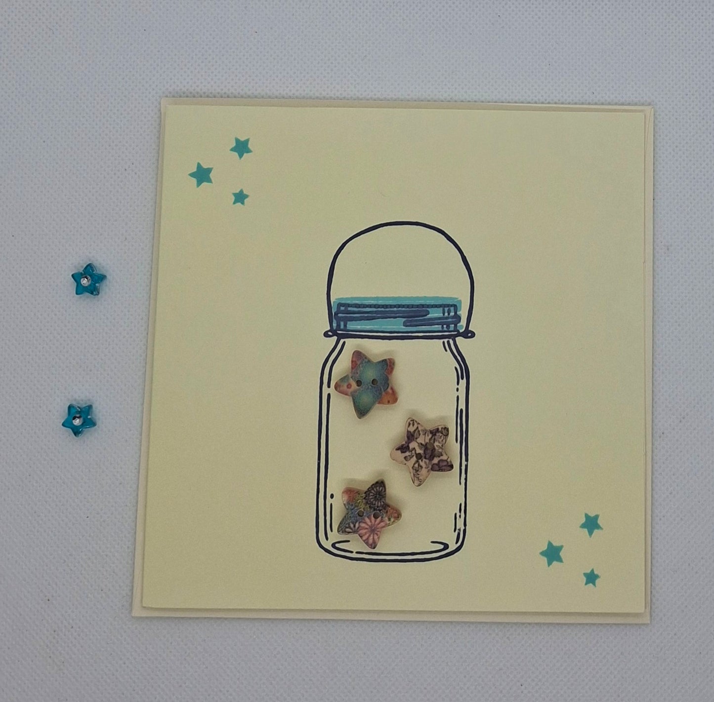 A handcrafted greeting card featuring a jar with star buttons inside, set against a yellow background with stamped stars.