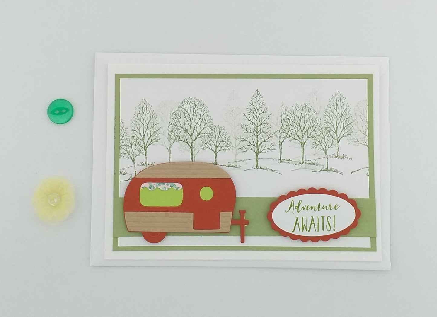 A cheerful a6 greeting card with a hand-stamped design featuring a red and white camper van in a green and brown landscape, titled 'Adventure Awaits'.