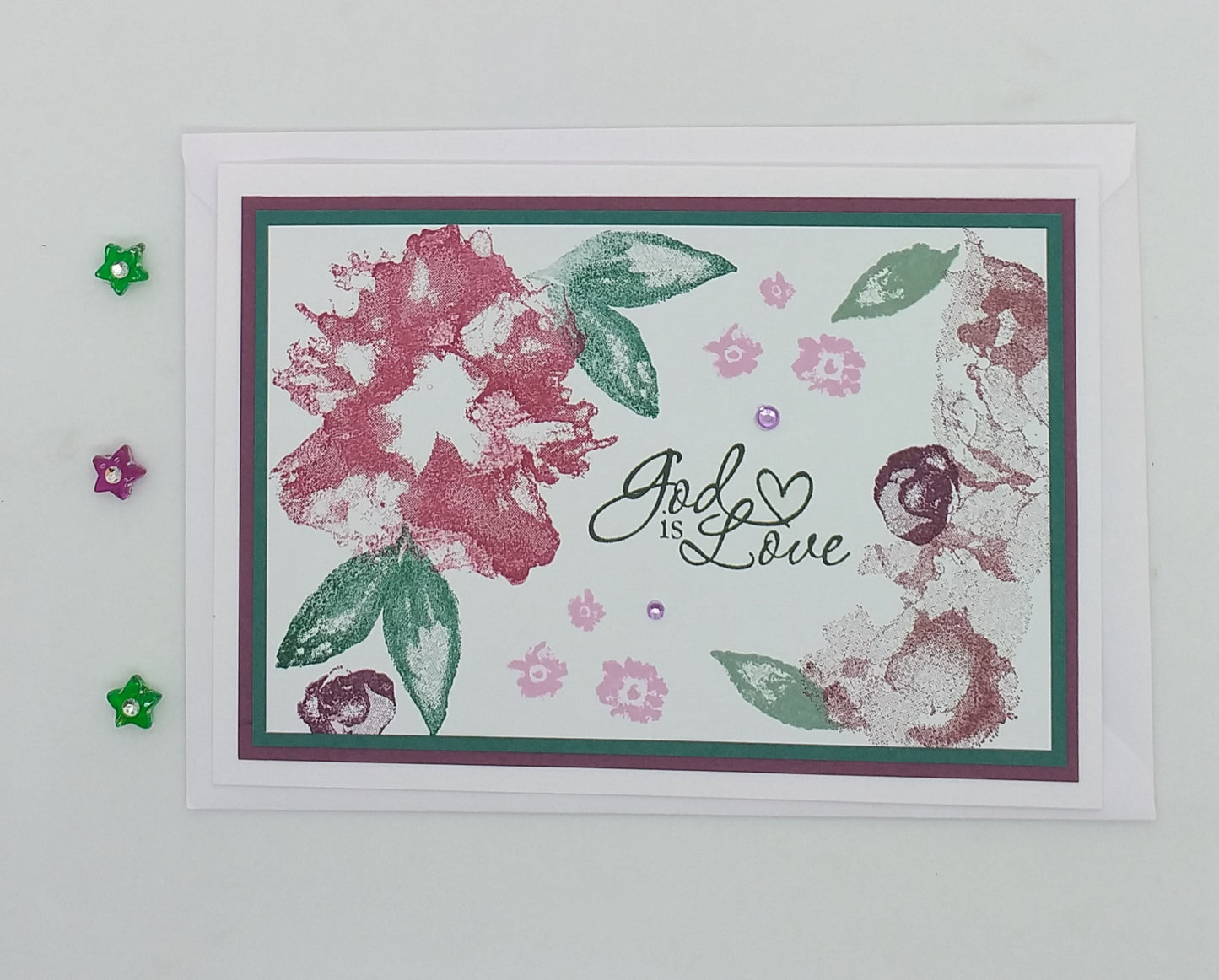 A6 card with hand-stamped design featuring a pink and green color scheme and the text 'God is Love' along with floral patterns and stars.