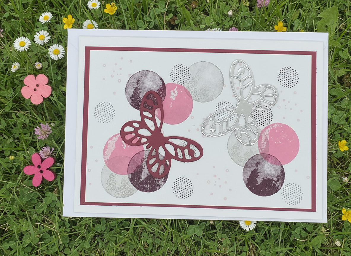A colorful greeting card with a pattern of butterflies and circles, accompanied by a pink envelope and decorative flowers.