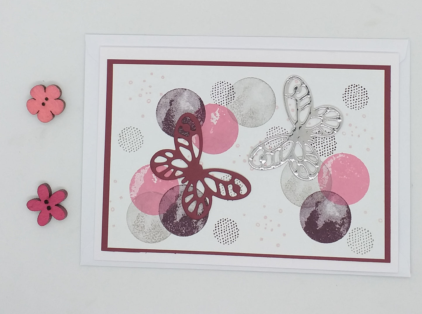 A colorful greeting card with a pattern of butterflies and circles, accompanied by a pink envelope and decorative flowers.