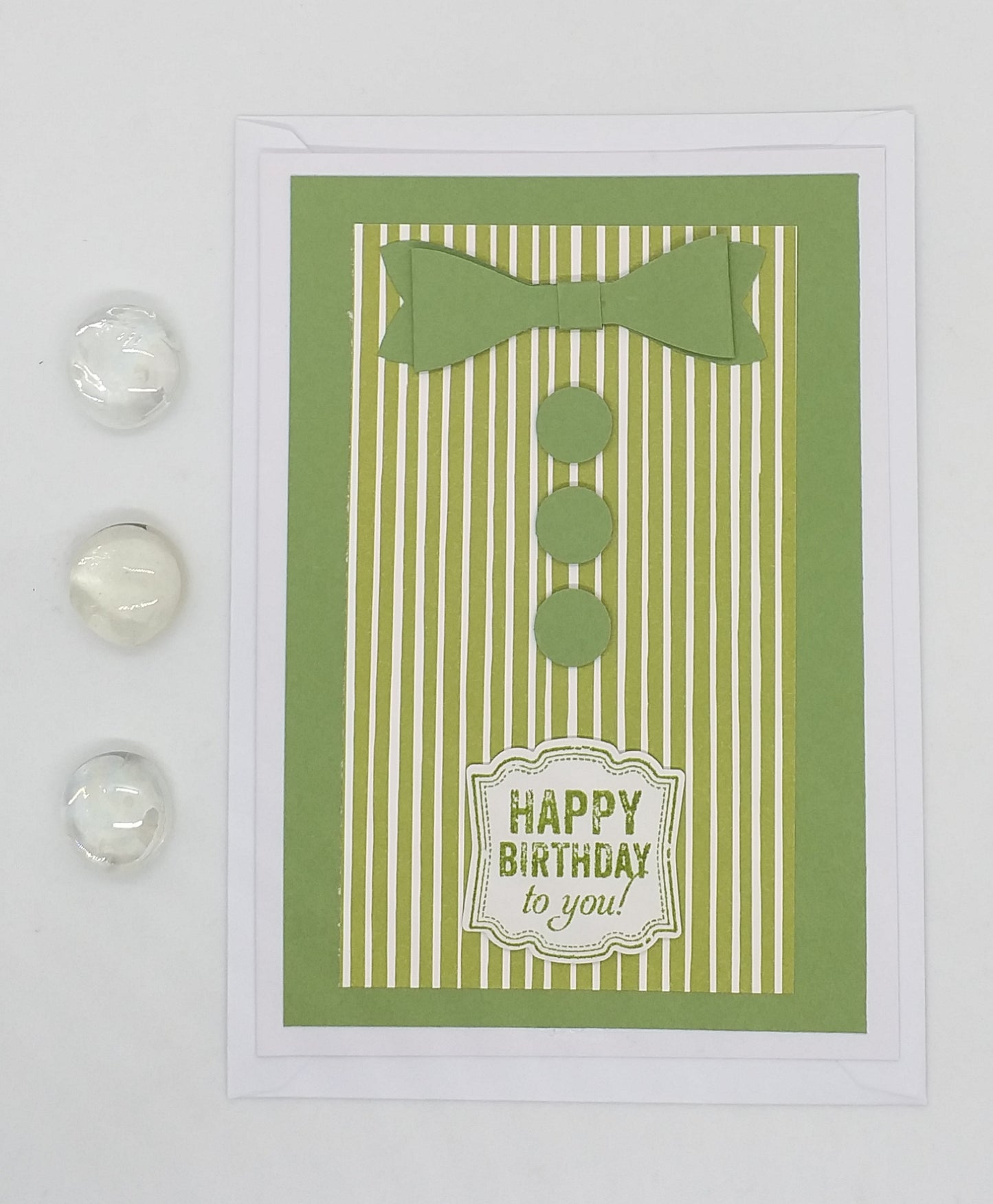 Greeting card with green shirt design, watch, cufflinks, and pen on a dark surface
