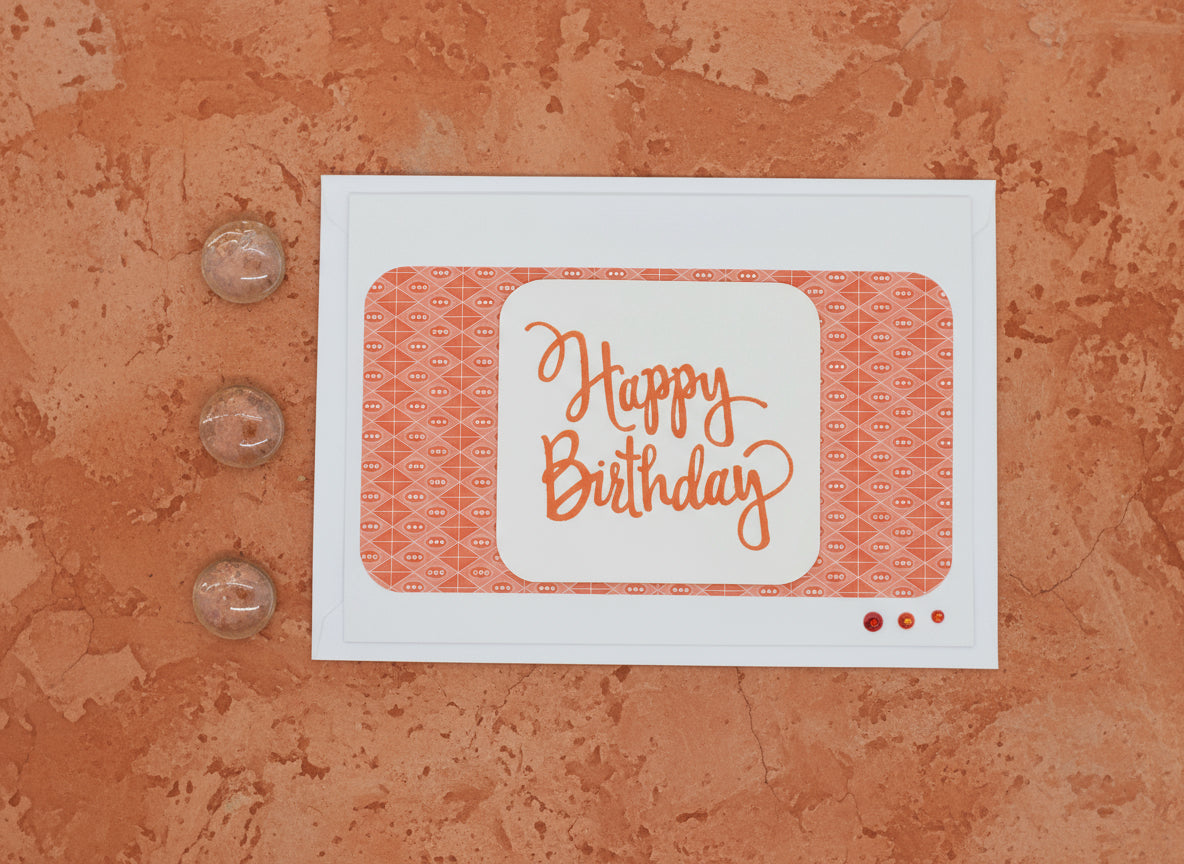 White card with 'Happy Birthday' text on a textured orange surface