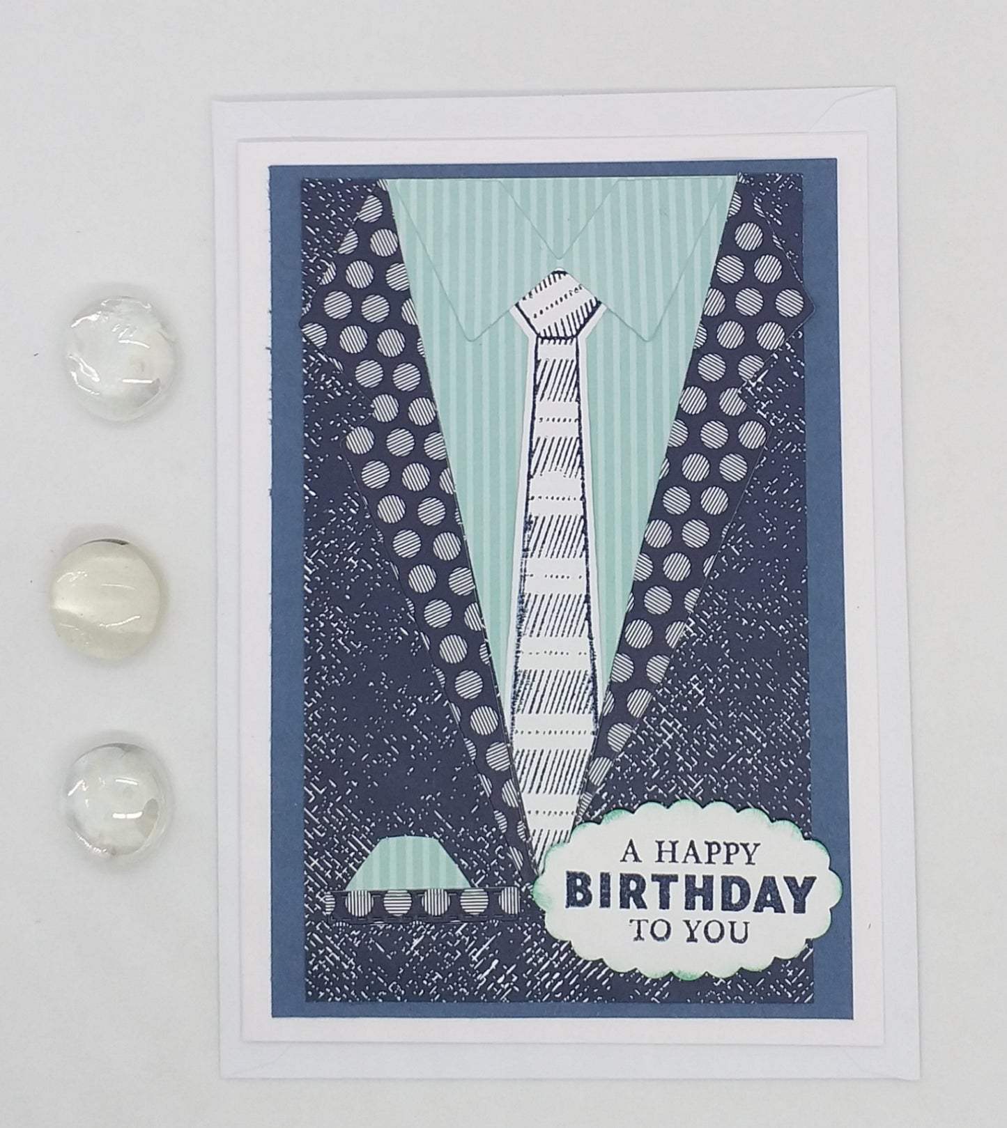 A folded a6 birthday card with a blue background featuring a graphic of a suit and tie, along with an envelope. The card has a blank inside for a personal message.