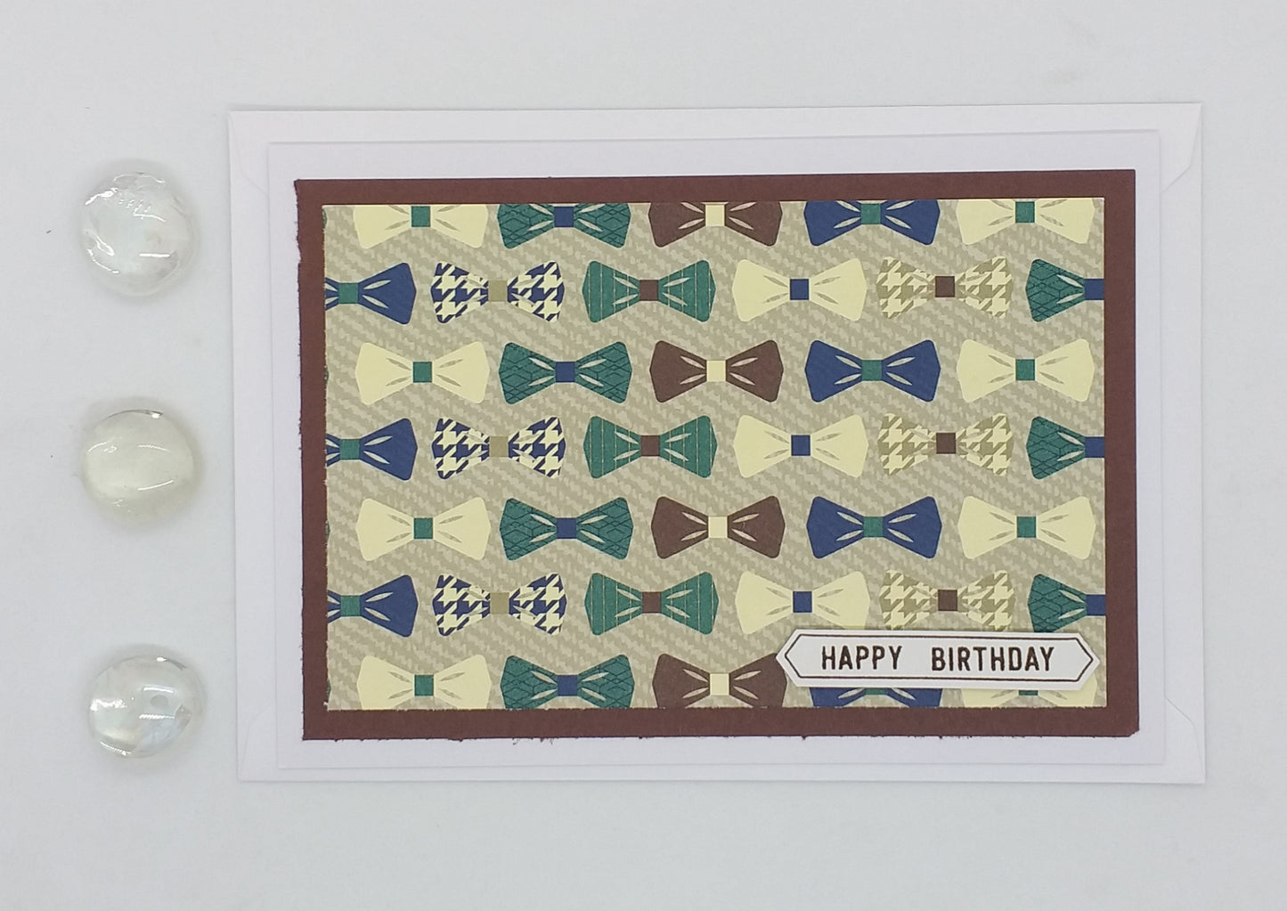 A colorful birthday card featuring patterns of bowties with a 'Happy Birthday' message, accompanied by an envelope and two loose bowtie designs in the corner.