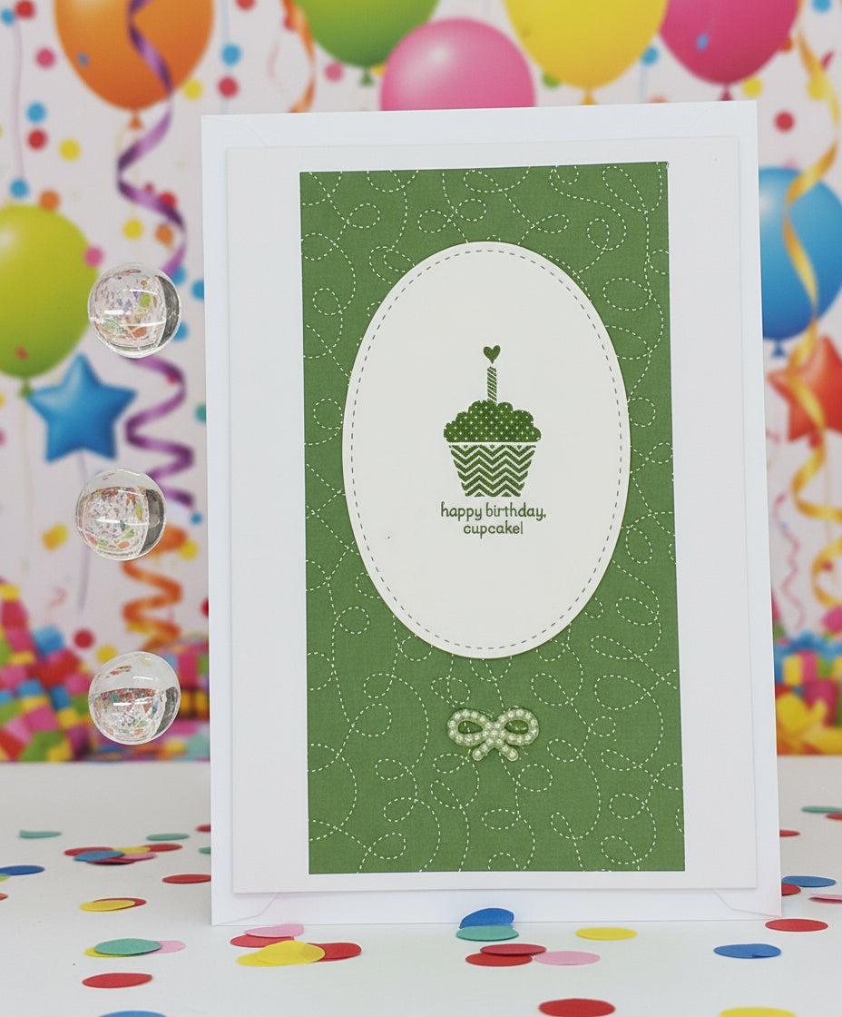 A green birthday card with a hand-stamped cupcake design, accompanied by a small envelope and decorative elements on the side.