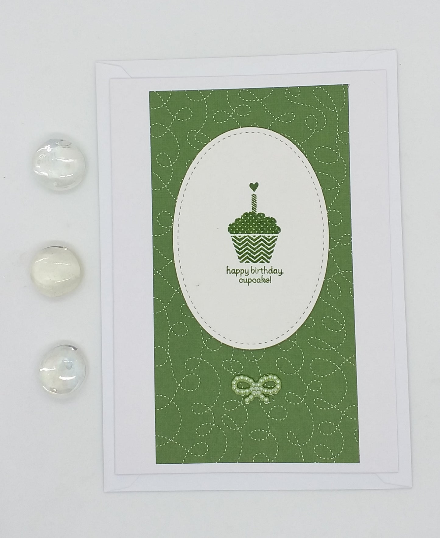 A green birthday card with a hand-stamped cupcake design, accompanied by a small envelope and decorative elements on the side.