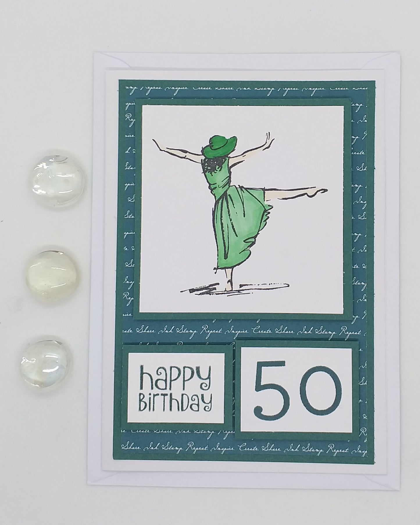 A handcrafted birthday card with a green and white color scheme, featuring a stamped image of a dancing lady, the number 50, and the text 'Happy Birthday'. The card is accompanied by two transparent embellishments.