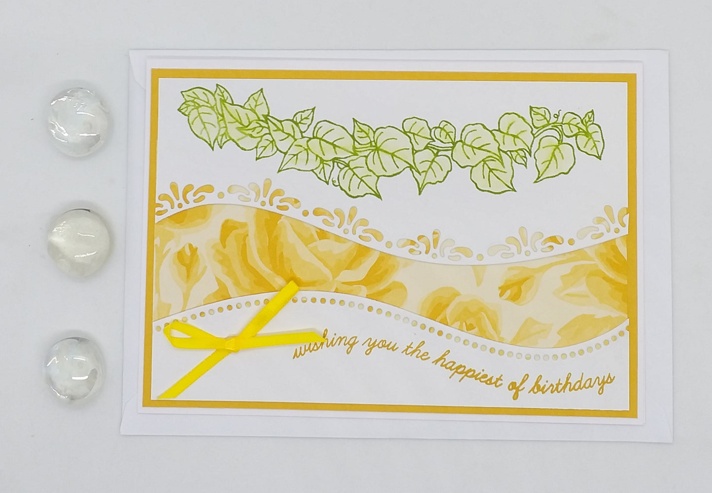 Hand-stamped birthday card with a yellow and green floral design and the text 'Happy Birthday' on it, displayed on a white background with decorative elements.