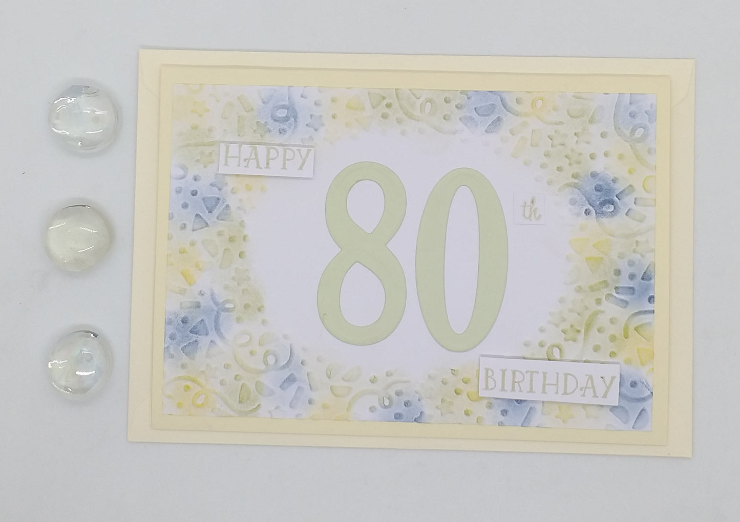 A colorful embossed birthday card with the number 80 and the words 'Happy 80th Birthday' on the front, accompanied by three decorative seals.