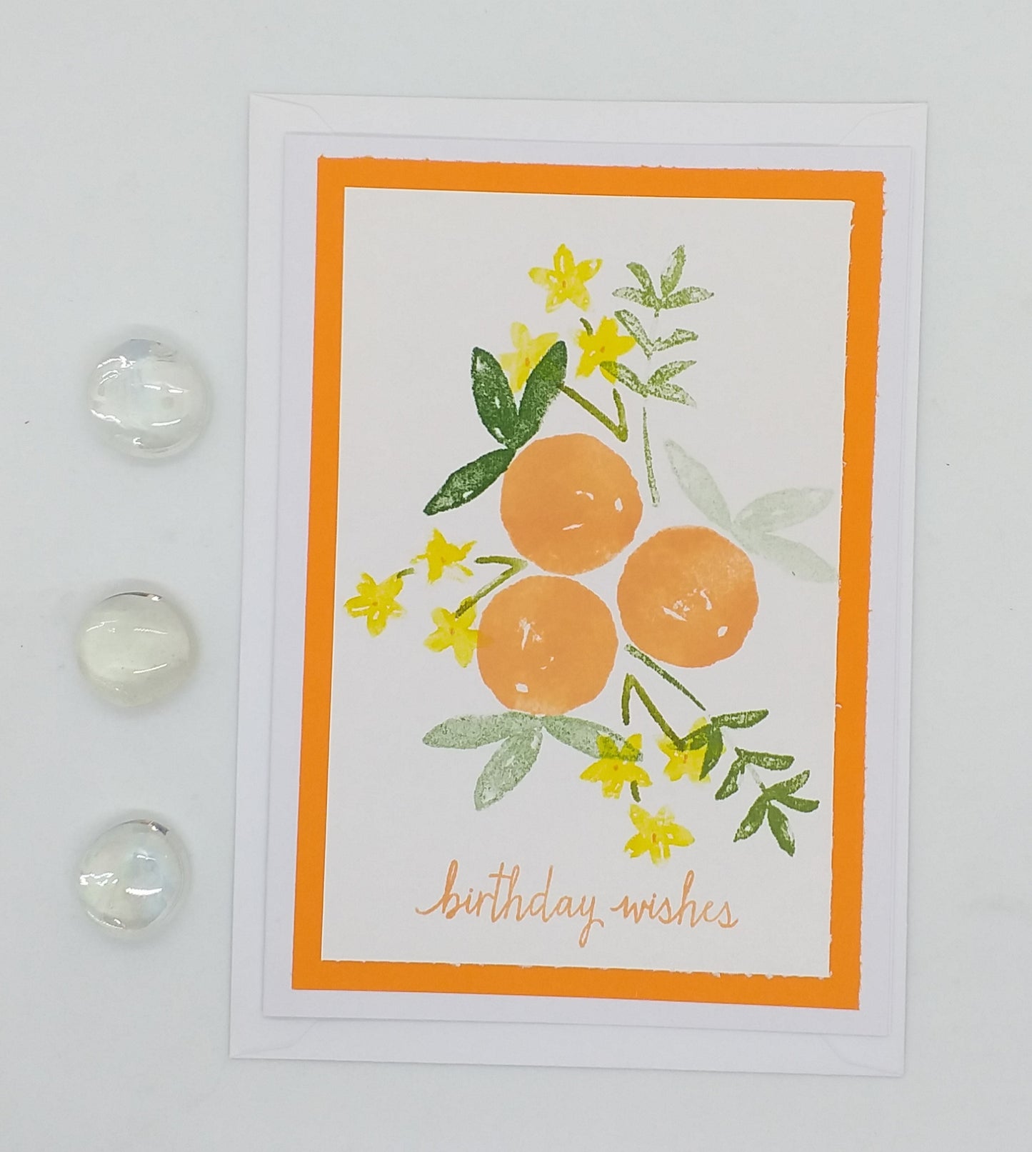 Hand stamped and layered a6 card with an orange background, featuring illustrations of orange blossoms and green leaves, and the text 'Happy Birthdays'.