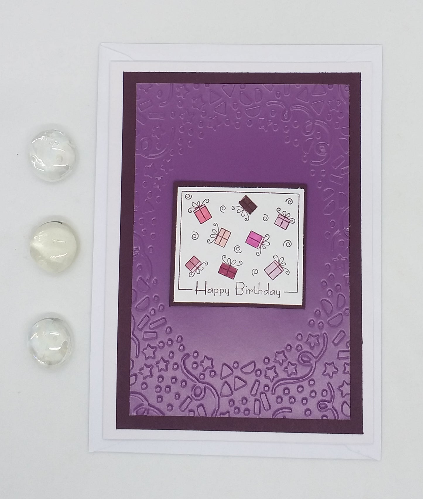 A purple birthday card with a hand-stamped, embossed design and the words 'Happy Birthday' displayed. The card is accompanied by two clear embellishments on the side.