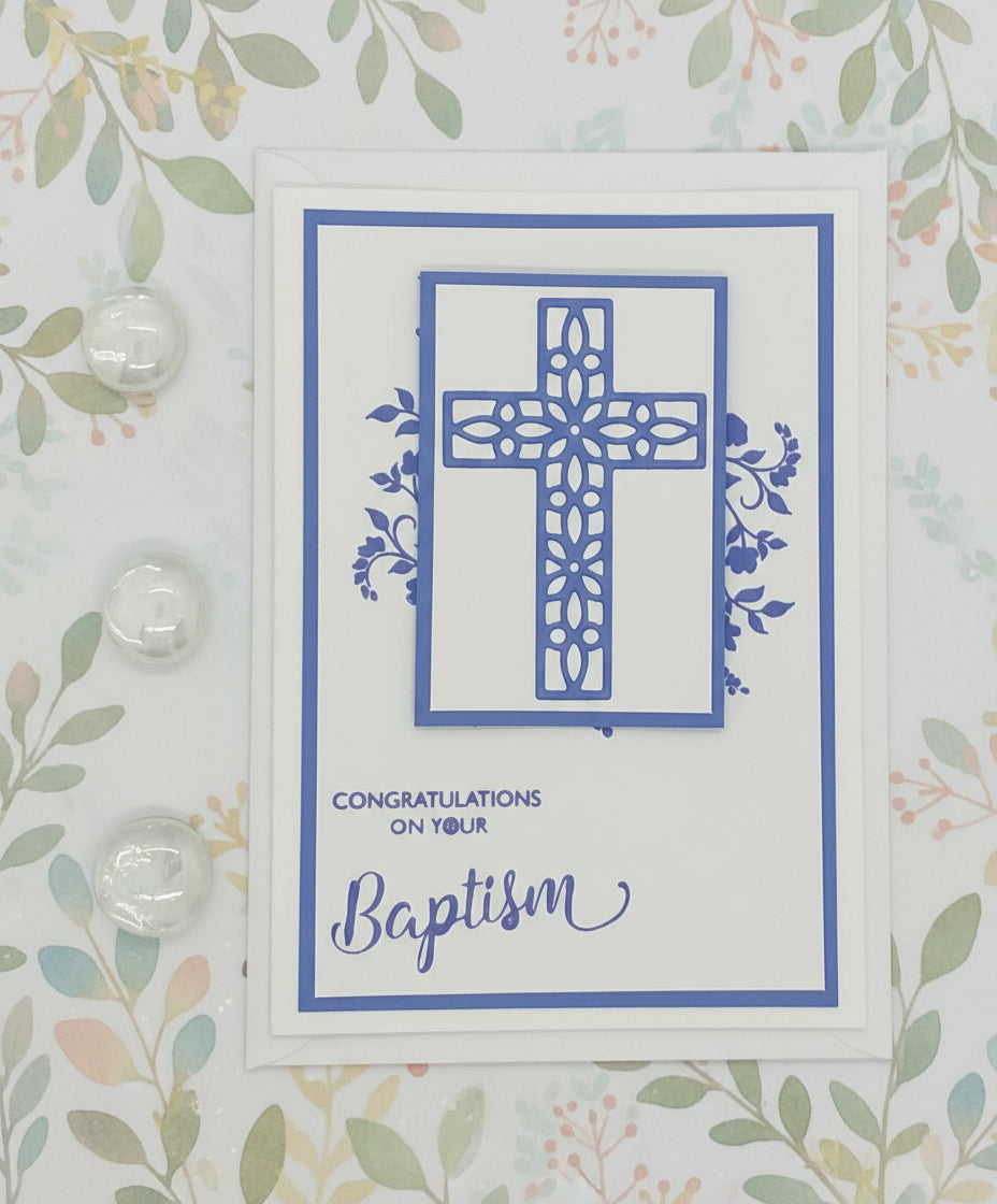 Greeting card with blue cross design and 'Congratulations on your Baptism' text on a floral patterned background.