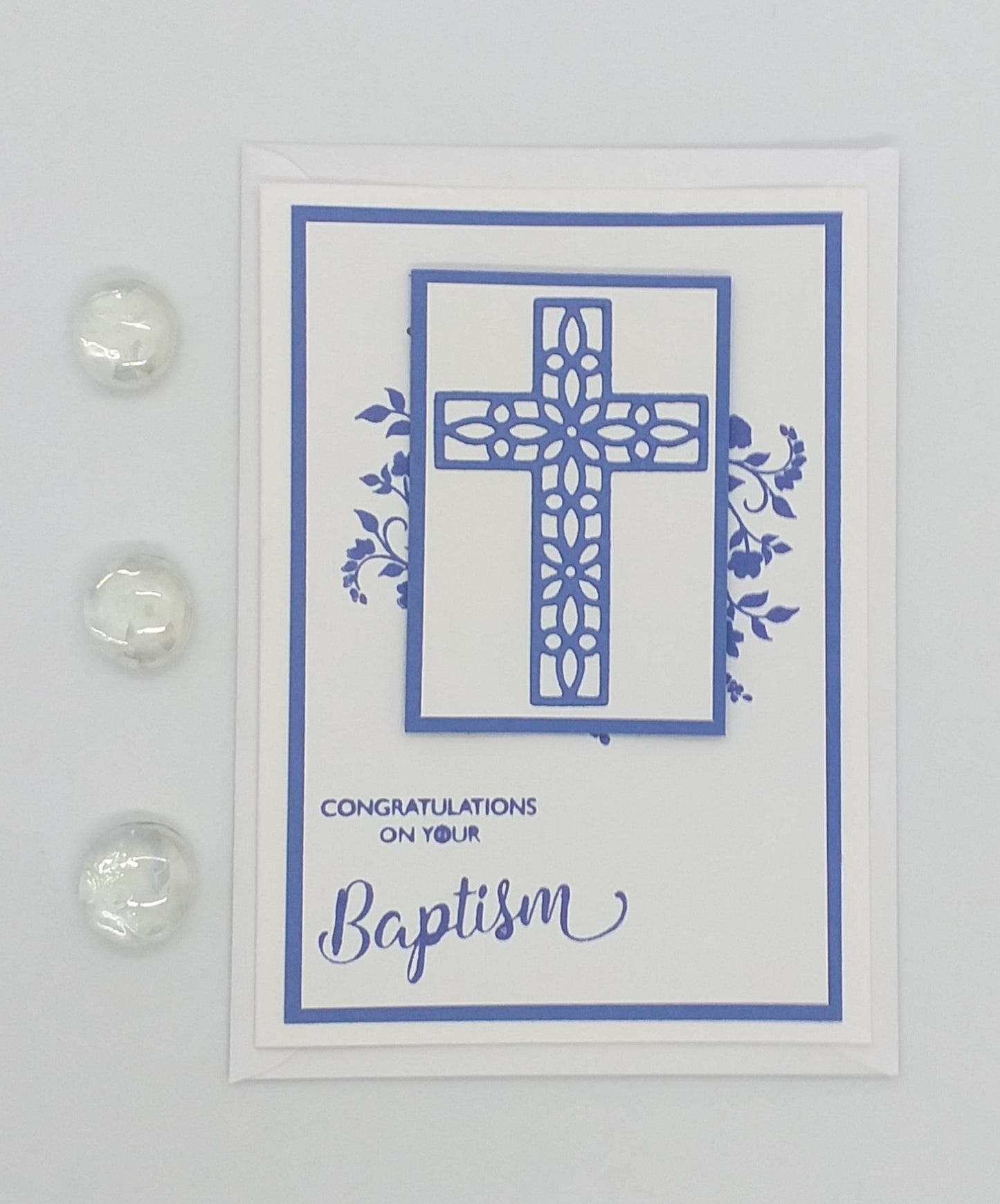 Greeting card with blue cross design and 'Congratulations on your Baptism' text on a floral patterned background.