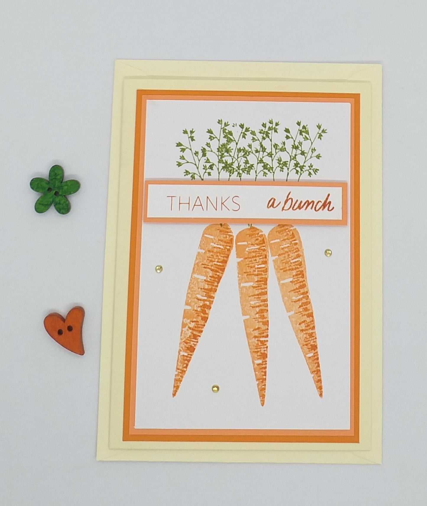 A hand-stamped greeting card with orange and green floral patterns and text reading 'THANKS a bunch', accompanied by an envelope and decorative buttons.