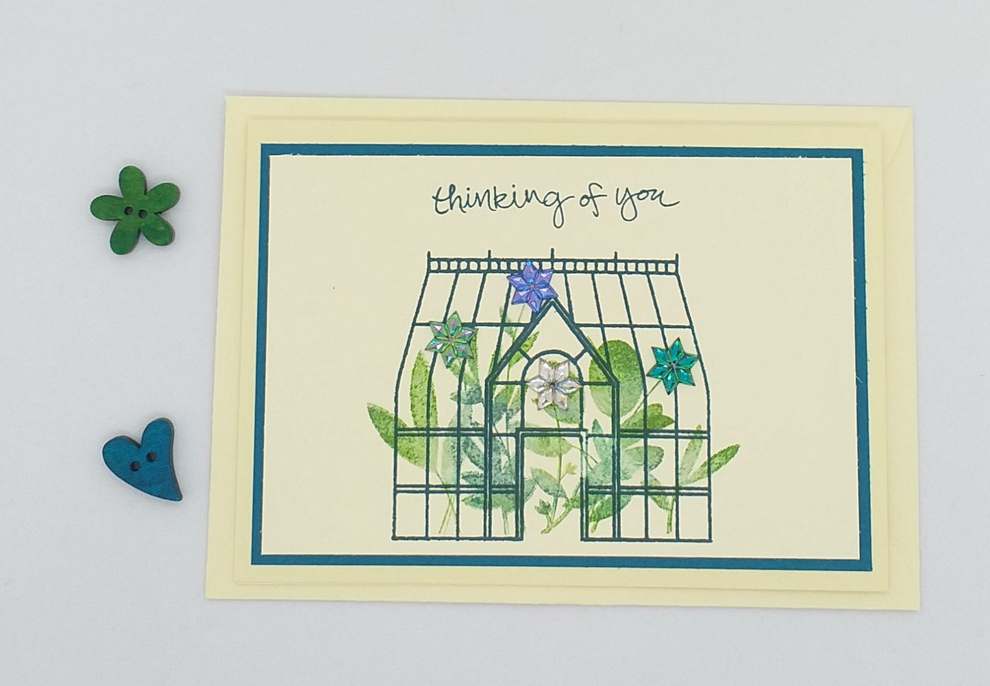A greeting card with a greenhouse design, titled 'Thinking of You', accompanied by an envelope and decorative elements.