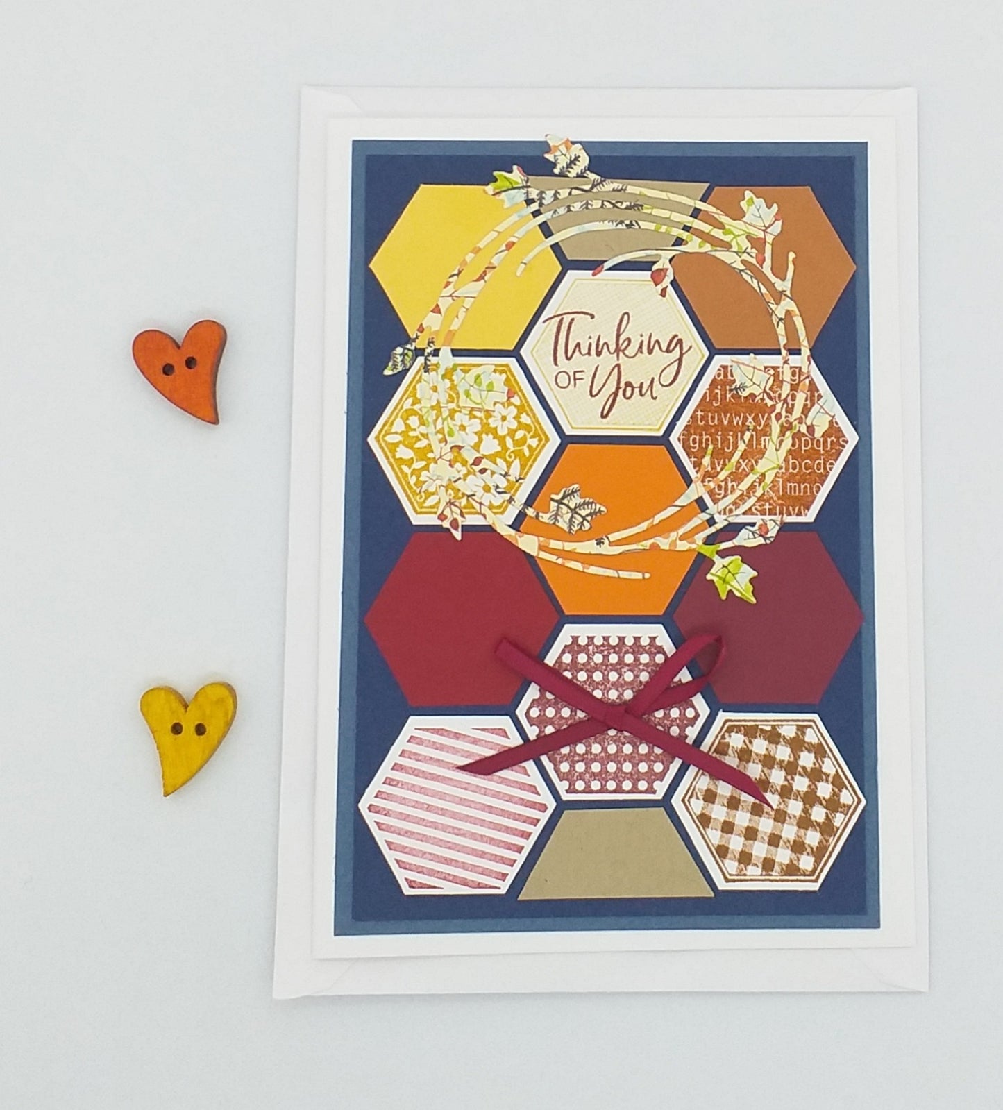 A colorful greeting card with hand-stamped details, a die cut wreath, and a red ribbon, accompanied by a small orange heart-shaped decoration.
