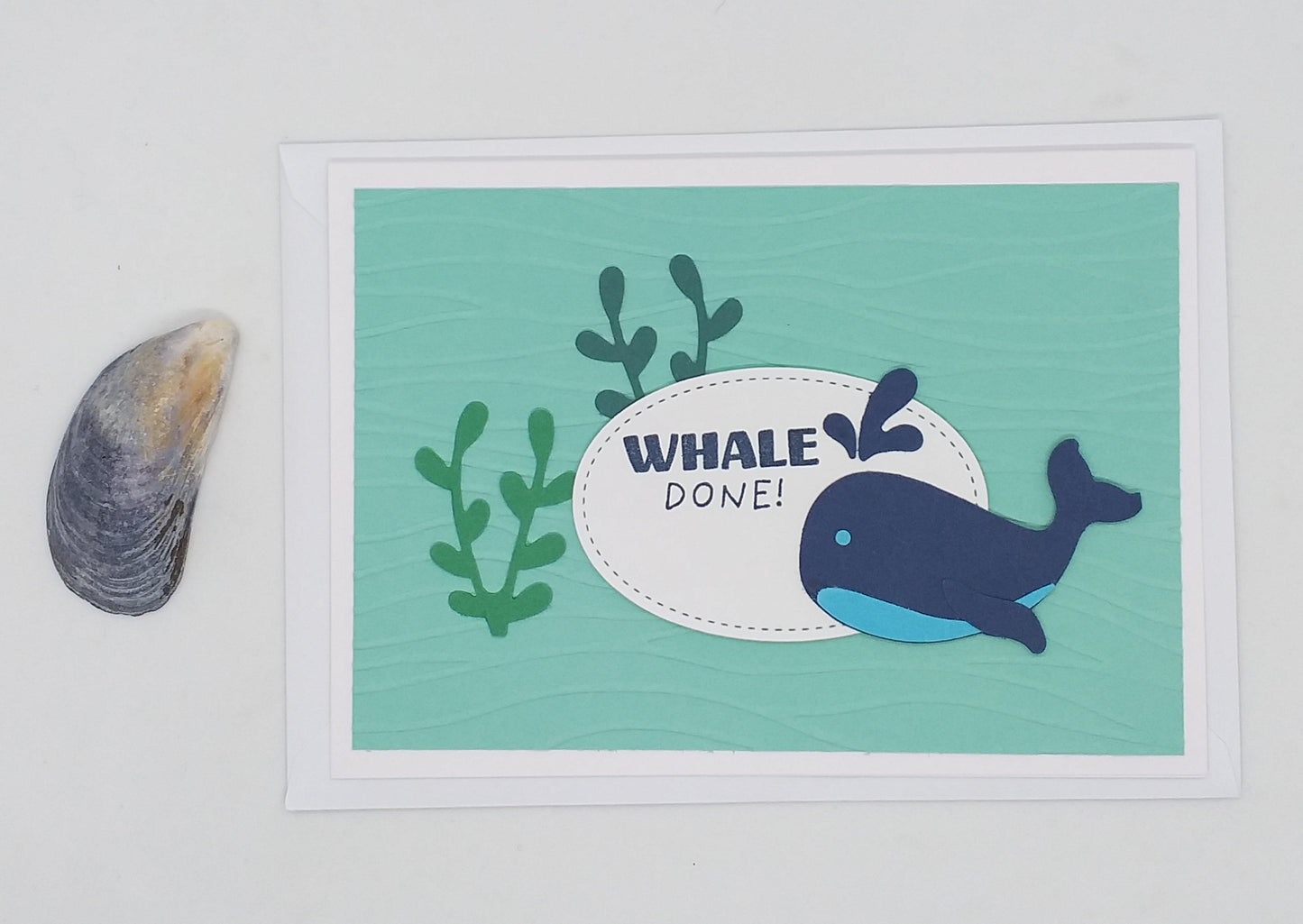 A 'Whale Done' greeting card with a cartoon whale and seaweed design, accompanied by a seashell to the left.