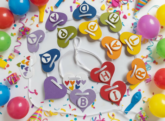 Colorful heart-shaped letter cookies on a white plate with balloons and streamers in the background.