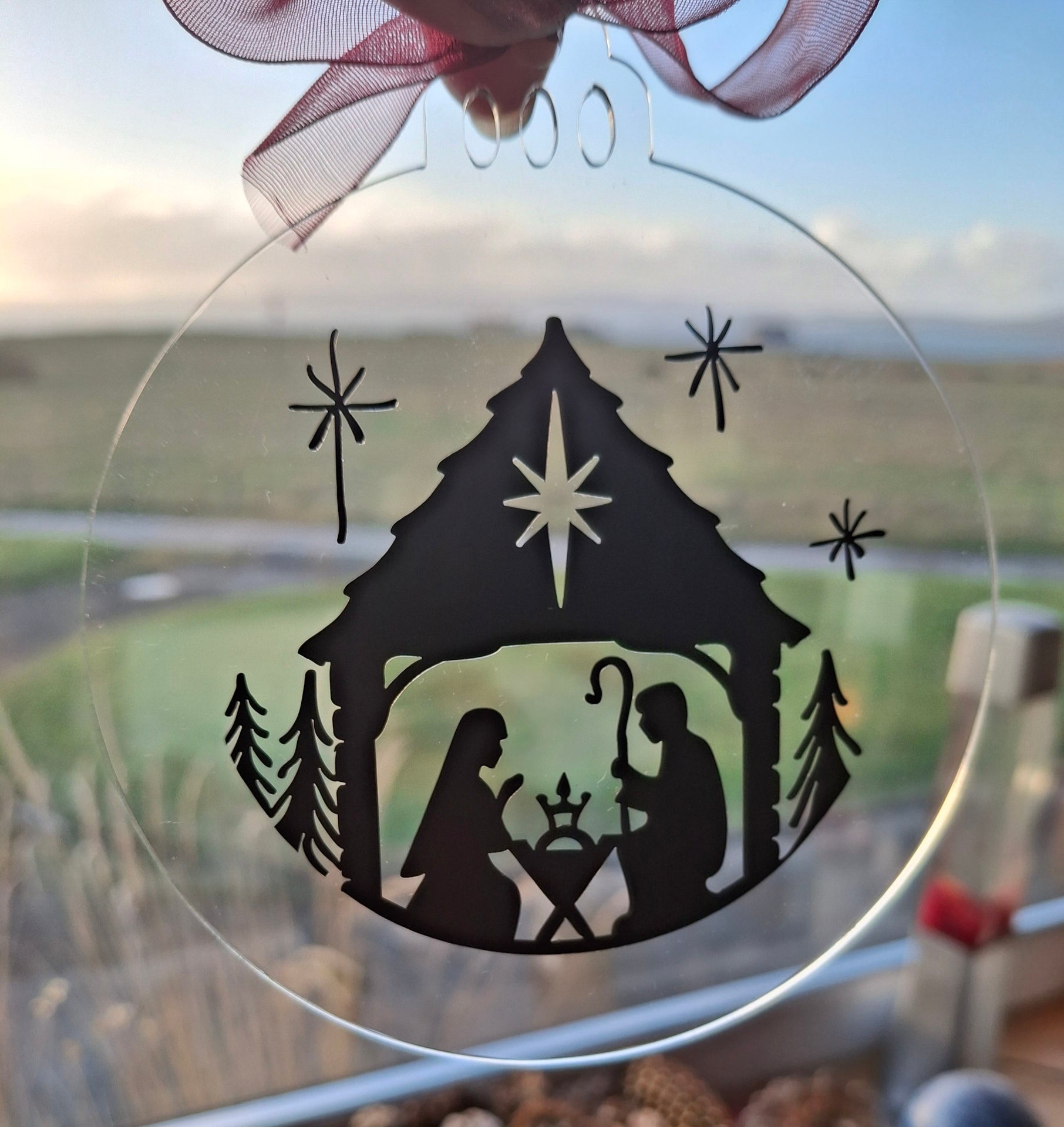 Decorative Christmas nativity scene hanging on a window with a blurred outdoor background.