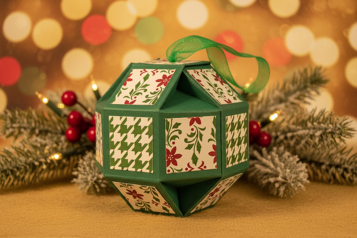 A handmade geometric paper ornament in dark green, decorated with panels featuring red floral patterns and green-and-white houndstooth designs, topped with a sheer green ribbon.
