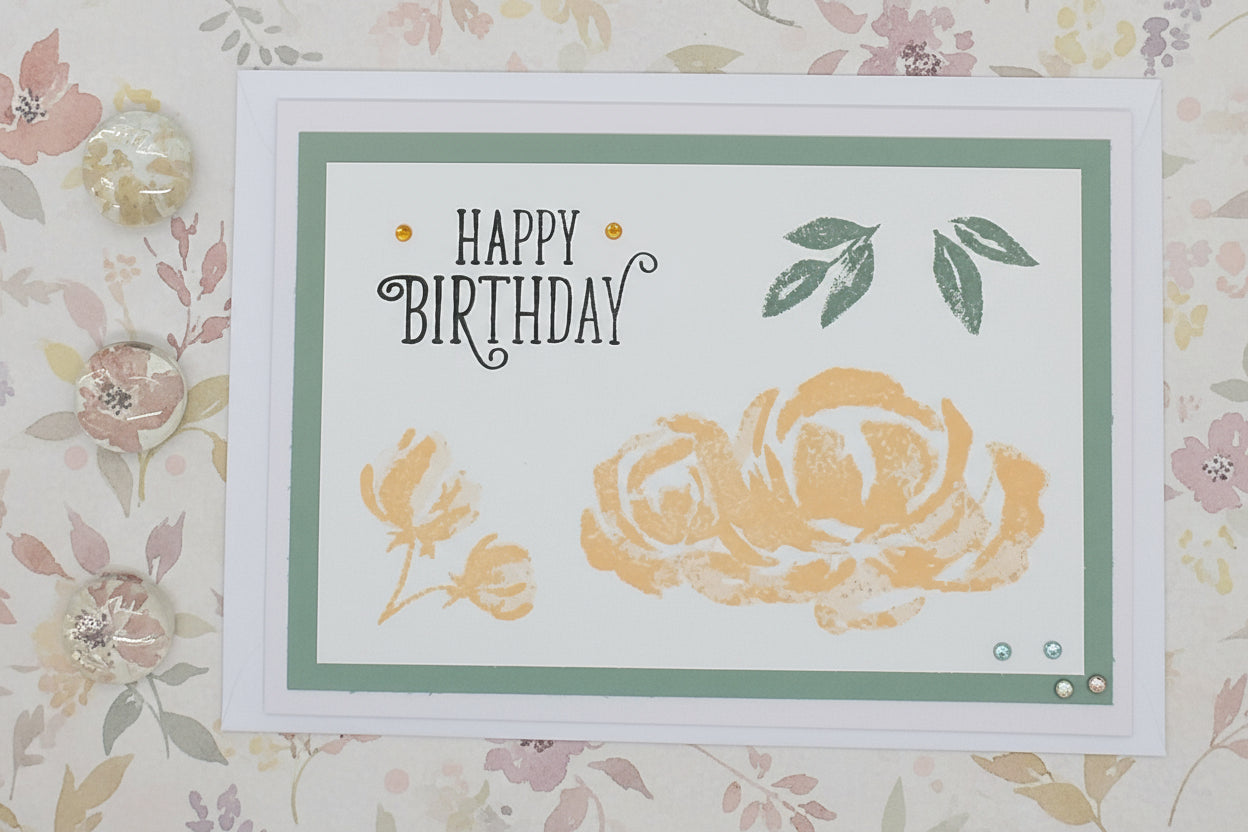 A hand-stamped a6 birthday card with 'Happy Birthday' text, floral designs, and a stamped envelope on a white background.