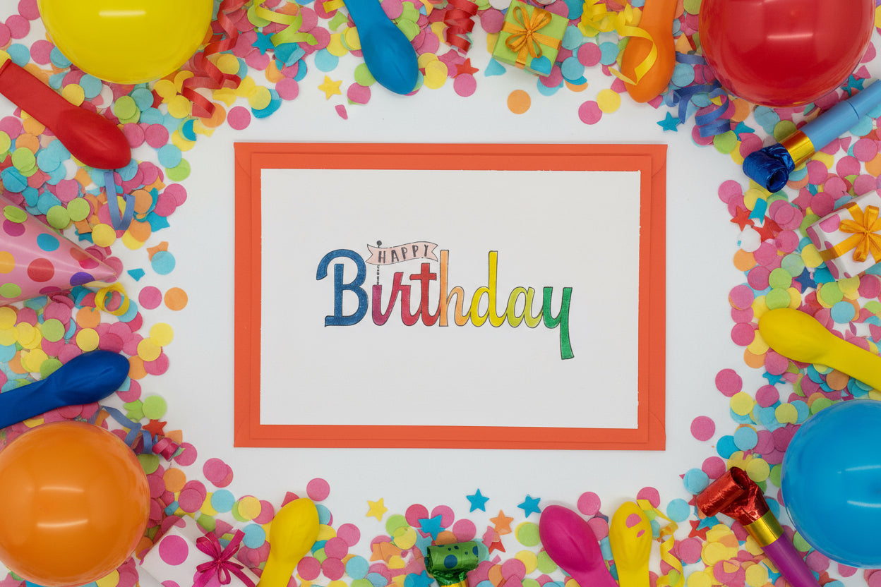 A vibrant birthday card with a colorful 'Happy Birthday' greeting in a Display font, presented with a red envelope and two decorative elements on the side.