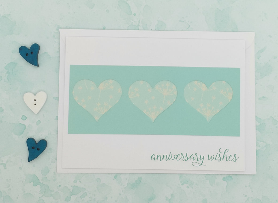 Card with three hearts and 'anniversary wishes' text on a light blue background