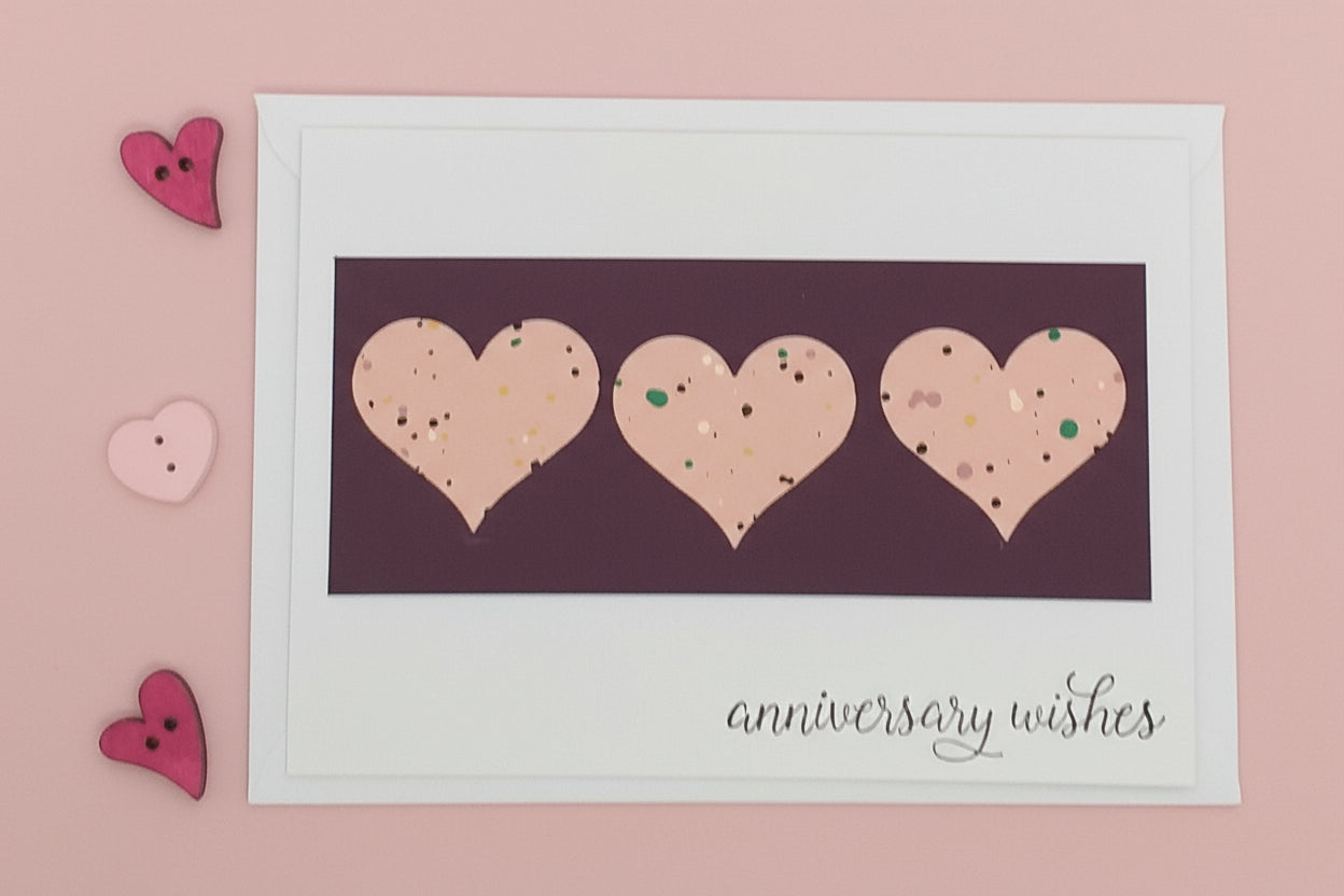Framed card with three heart shapes and 'anniversary wishes' text on a pink background.